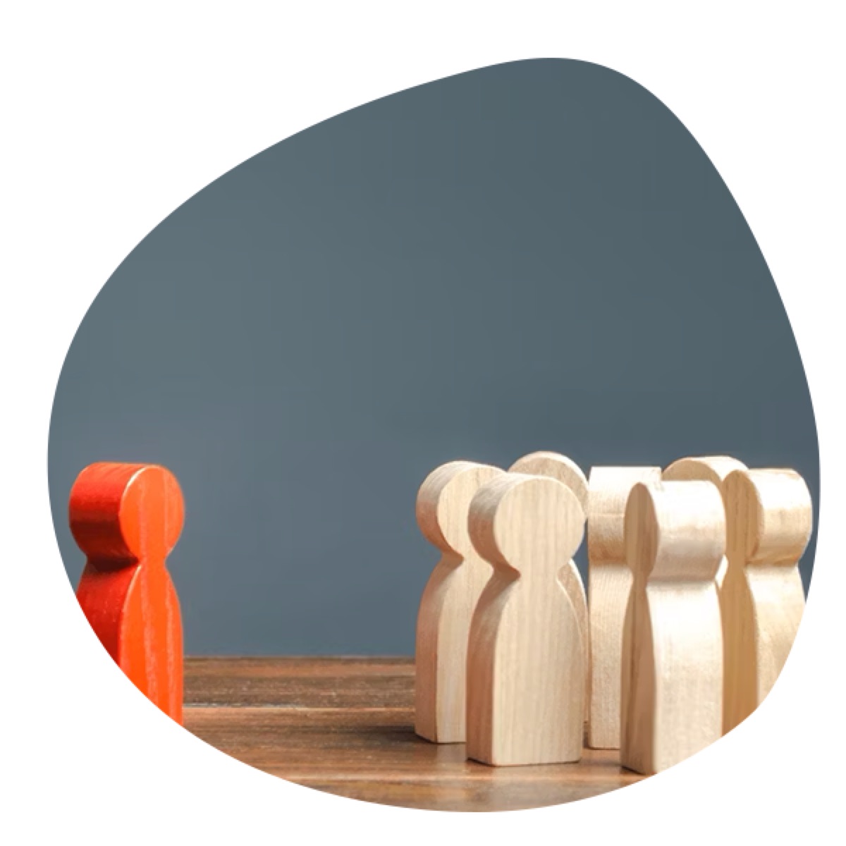 A red wooden figure standing alone, facing a group of light wooden figures